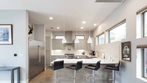 Een moderne keuken met een centraal eiland, roestvrijstalen apparatuur en drie barkrukken.