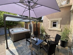 Un patio exterior con jacuzzi, mesa, sillas y un paraguas grande.