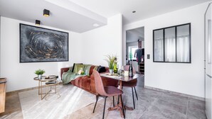 A modern living room with a large abstract painting, a brown sofa, a dining table with chairs, and a small side table with a plant. - Gîte confort de la Fontaine de Jonquier (Seguret)