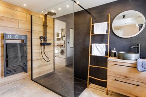 Un baño moderno con ducha de vidrio, una escalera de madera, un espejo redondo y un tocador de madera con lavamanos.