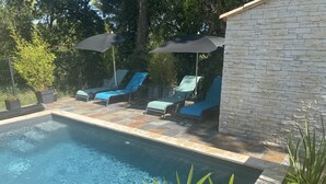 A swimming pool with lounge chairs and umbrellas, surrounded by a stone wall and greenery. - Gîte confort de la Fontaine de Jonquier (Seguret)