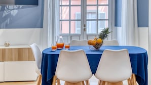 A dining area with a blue tablecloth, two white chairs, a fruit bowl, and a pitcher of orange juice. - IzzHome Corso76 (Cagliari)
