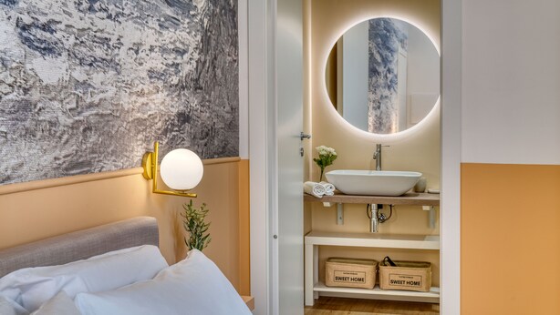 A modern hotel room with a bed, a round mirror with a light, a white sink, and storage boxes labeled "SWEET HOME". - IzzHome Corso76 (Cagliari)