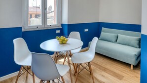 A modern living room with a blue and white color scheme, a round table with chairs, a sofa, and a hanging light fixture. - IzzHome Corso76 (Cagliari)