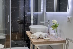 A modern bathroom with a glass shower enclosure, a white sink, and a wooden vanity. - IzzHome Corso76 (Cagliari)