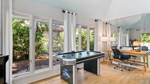 Ein Zimmer mit Kicker, Schreibtisch und Computer sowie großen Fenstern.