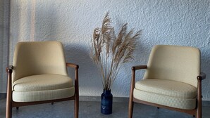 Two checkered armchairs with wooden legs and a vase with dried plants on a tiled floor against a textured wall with two wall-mounted lights. - Vahide Dalyan (Cesme)