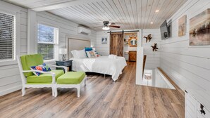 A bedroom with a bed, a green chair, a wooden floor, and a ceiling fan. - Allie’s on the Rocks Pet-Friendly Lakefront Bungalow (Cullman)