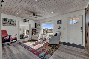 A room with a wooden ceiling, a large window with a view, a red rocking chair, and a patterned rug.