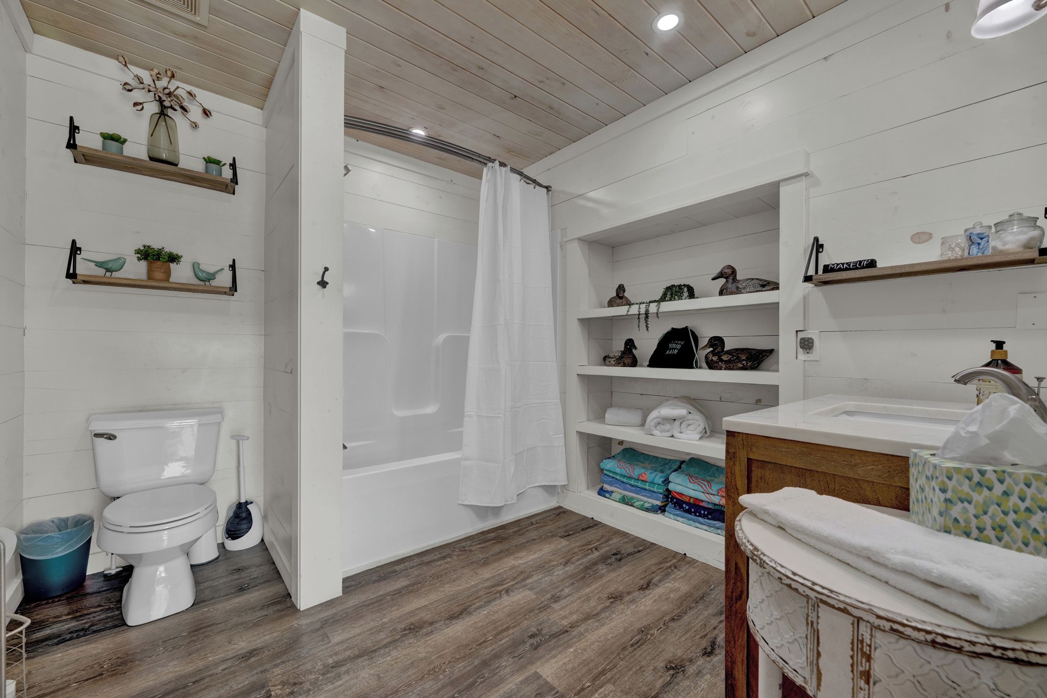 Une salle de bain comprenant des toilettes, une douche, des étagères avec des serviettes et un lavabo.