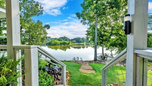 A view from a wooden deck overlooking a lake, with a metal railing and a stone path leading to the water. - Allie’s on the Rocks Pet-Friendly Lakefront Bungalow (Cullman)