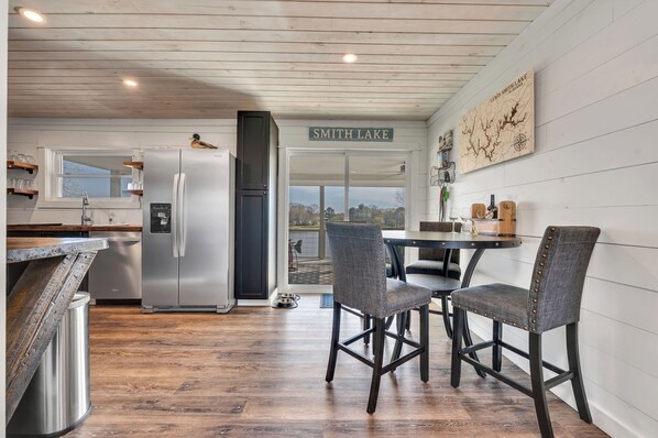 A modern kitchen with a stainless steel refrigerator, wooden flooring, and a view of Smith Lake. - Allie’s on the Rocks Pet-Friendly Lakefront Bungalow (Cullman)