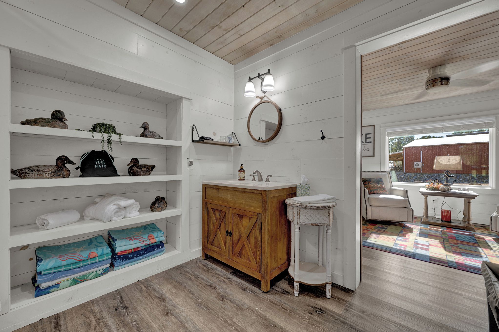 Un baño con tocador de madera, repisas con toallas y un espejo.