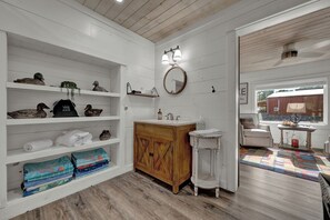 Een badkamer met een houten wastafelmeubel, planken met handdoeken en een spiegel.