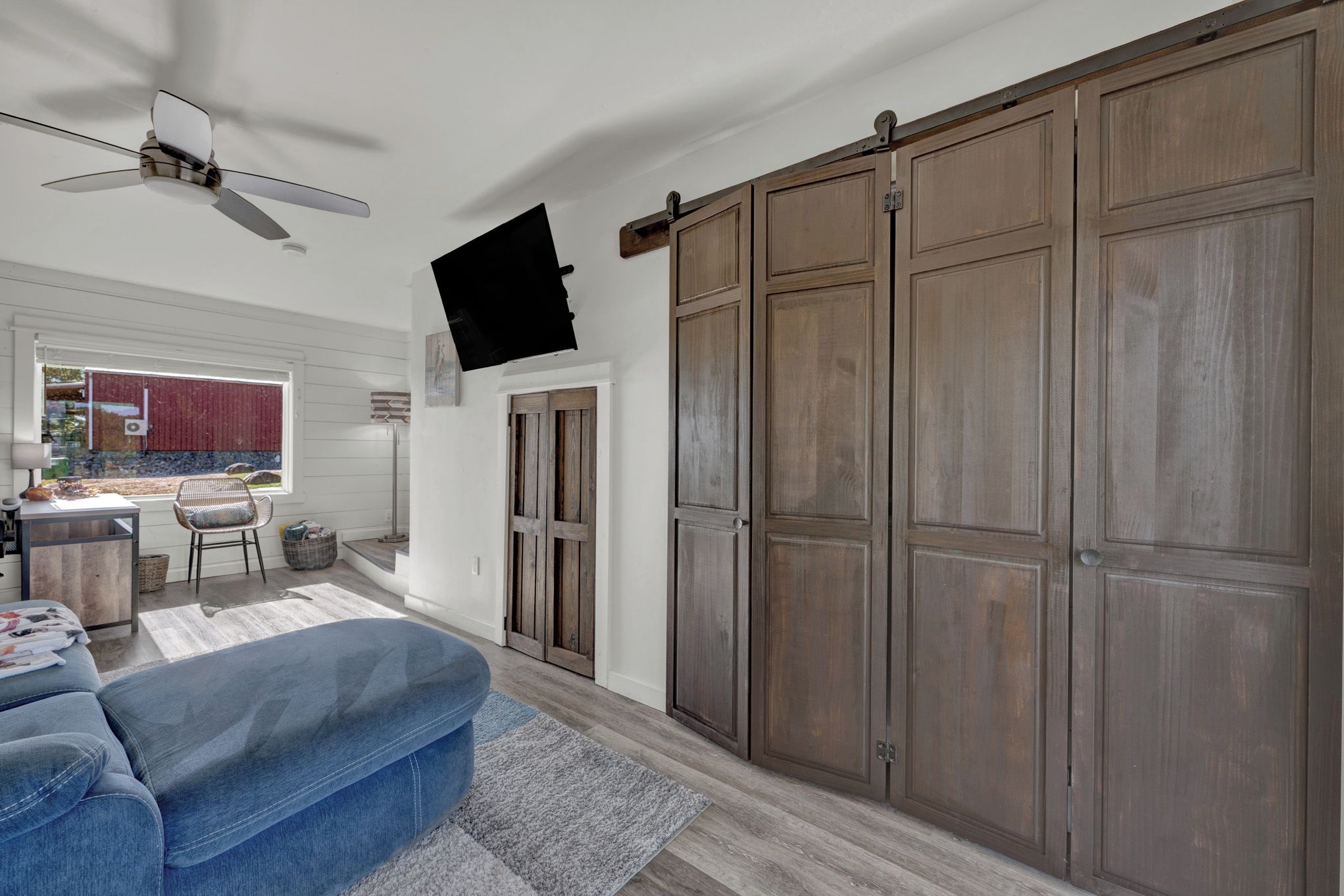 A room with a blue sofa, a ceiling fan, a sliding door, and a television mounted on the wall.