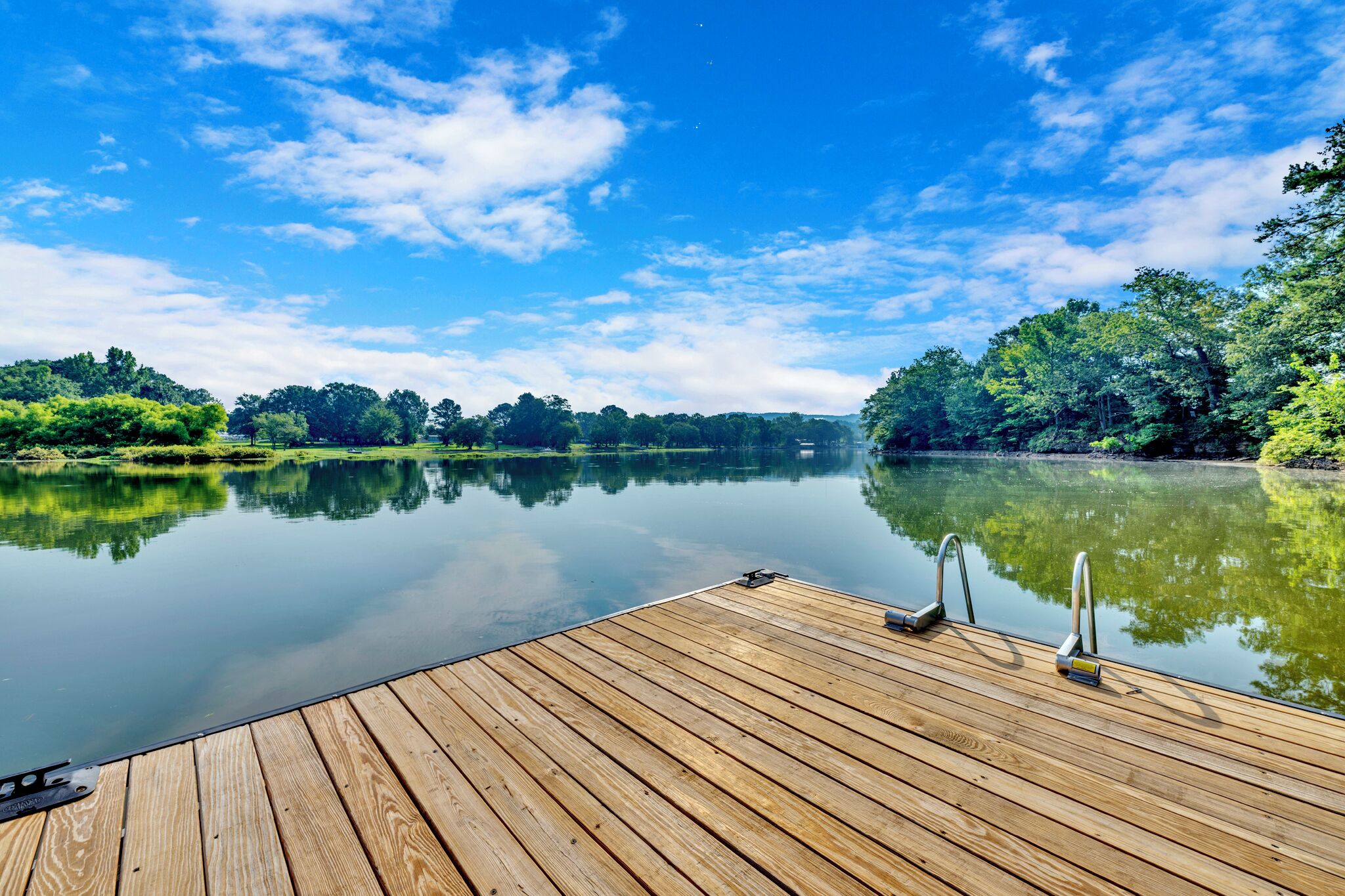 Une jetée en bois s’étendant au-dessus d’un lac paisible, avec des arbres en arrière-plan et un ciel dégagé.