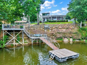 A lakeside property with a wooden dock, a stone retaining wall, and a modern house with a balcony. - Allie’s on the Rocks Pet-Friendly Lakefront Bungalow (Cullman)