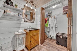 A bathroom with a wooden vanity, a sink, a mirror, and shelves with toiletries. - Allie’s on the Rocks Pet-Friendly Lakefront Bungalow (Cullman)