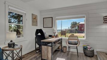 Quarto com escrivaninha, cadeira e vista para o exterior.