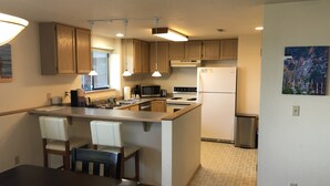 Cocina compacta con gabinetes de madera, una isla central con sillas, microondas, estufa y refrigerador.