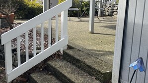 Un porche cubierto con barandilla blanca, escalones de piedra y un jardín con macetas, plantas y un banco.