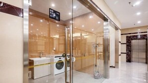 A modern hotel bathroom with a glass partition, a sink, a washing machine, and a vacuum cleaner. - Paibai Yun Hotel (Dalian Xianglujiao Light Rail Station Branch) (Dalian)