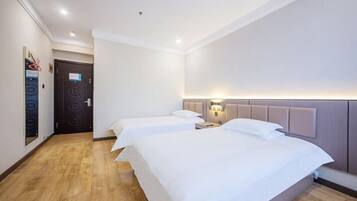 Quarto de hotel com duas camas, piso de madeira, uma porta e luminária fixada na parede.