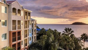 Ein mehrstöckiges Hotel mit Balkonen, die auf ein Gewässer und einen Sonnenuntergang blicken.