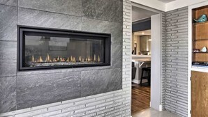 A modern fireplace with a stone facade, a kitchen area with wooden cabinets, and a dining space.