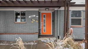 A house with a gray brick exterior, a bright orange door, and a small window.