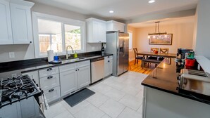 A modern kitchen with white cabinets, a stainless steel refrigerator, and a dining area with a table and chairs. - Outdoor Oasis: Unwind in the hot tub under twinkling lights in your private retreat! (Arvada)