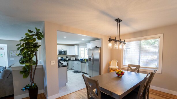 A modern kitchen with white cabinets, stainless steel appliances, and a dining area with a wooden table and chairs. - Outdoor Oasis: Unwind in the hot tub under twinkling lights in your private retreat! (Arvada)