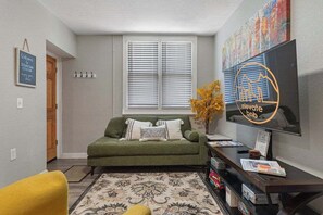 A living room with a green sofa, a flat-screen TV, a coffee table, and a decorative plant. - Family friendly in Downtown Littleton (Littleton)