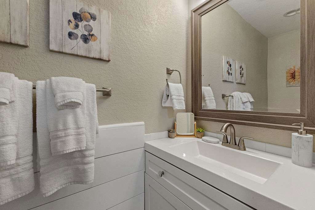 Un baño con un lavamanos blanco, un espejo grande y dos toallas colgadas en un perchero.