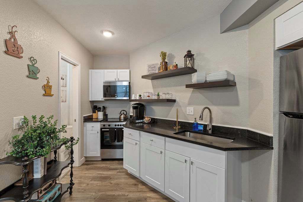 A modern kitchen with white cabinets, a black countertop, and stainless steel appliances. There are decorative items on the wall and shelves above the counter.