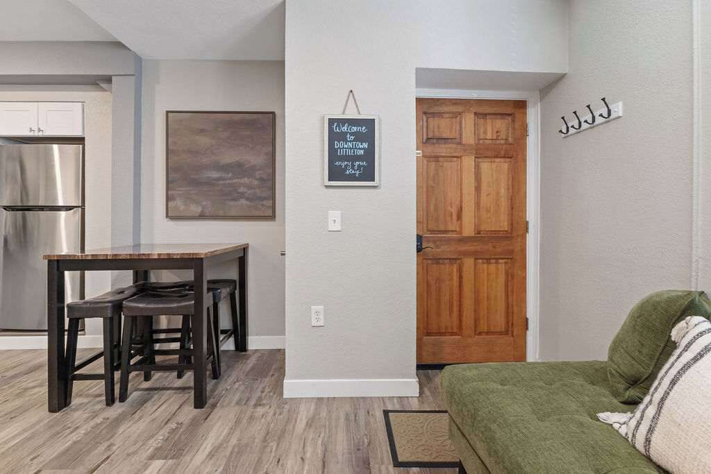 Una cocina moderna con un refrigerador de acero inoxidable, una mesa de comedor de madera con cuatro sillas, un letrero en la pared y una puerta de madera.