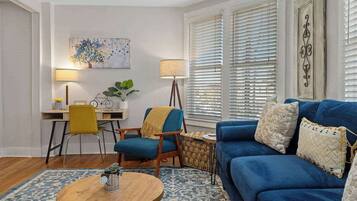 A living room with a blue sofa, a wooden coffee table, a yellow chair, and a desk with a lamp.