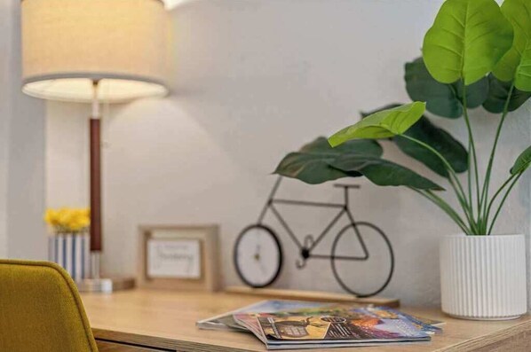 Una mesa de madera con una lámpara, un cuadro enmarcado, una bicicleta decorativa, una planta en maceta y una revista.