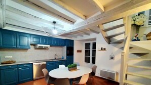 A kitchen with blue cabinets, a white dining table, and a spiral staircase. - Gîte Eloquent (Gratot)