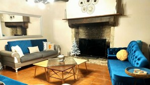 A living room with a fireplace, a sofa, a coffee table, and a TV. - Gîte Eloquent (Gratot)