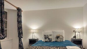 A bedroom with a bed, two nightstands, a window with curtains, and a door. - Gîte Eloquent (Gratot)