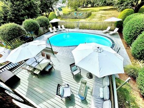 Une piscine entourée de chaises longues et de parasols, le tout installé sur une terrasse en bois.