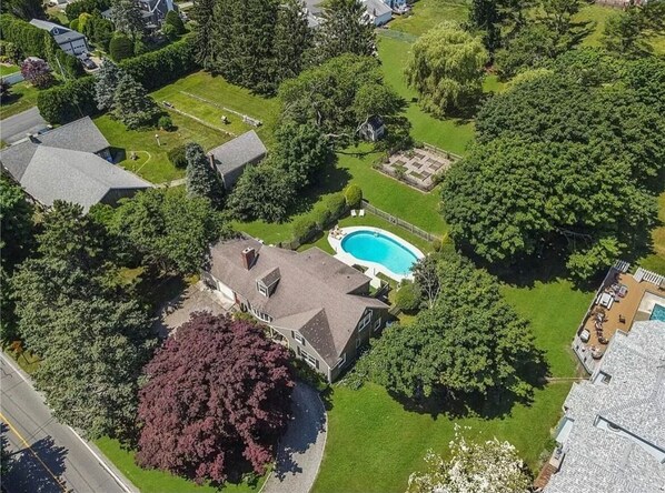 An aerial view of a residential property with a swimming pool, a large house, and surrounding greenery.