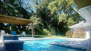 A swimming pool with a tiled deck, a covered seating area, and surrounding greenery. - Book a Paradise for your Family's Florida Vacation!  (Clearwater)