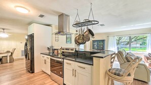 A modern kitchen with white cabinets, stainless steel appliances, and a hanging pot rack. - Book a Paradise for your Family's Florida Vacation!  (Clearwater)
