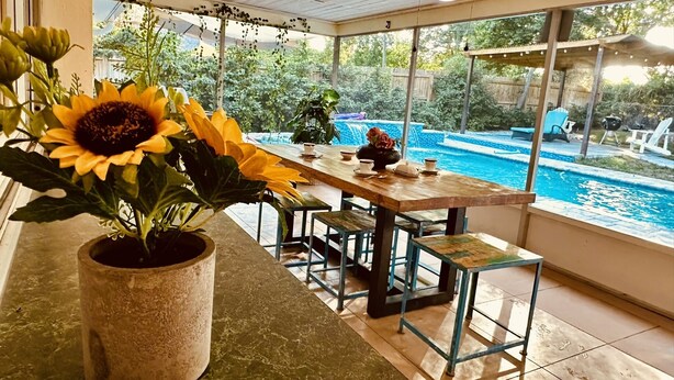 A covered patio with a pool view, a table with chairs, and a large sunflower plant. - Book a Paradise for your Family's Florida Vacation!  (Clearwater)