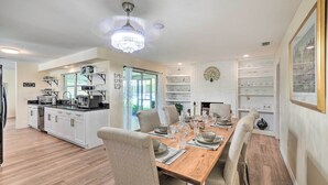 A modern kitchen with white cabinetry, a wooden dining table set for six, and a chandelier. - Book a Paradise for your Family's Florida Vacation!  (Clearwater)