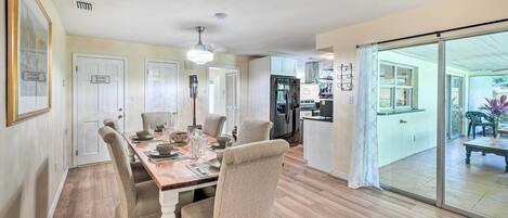 A dining area with a wooden table set for four, surrounded by upholstered chairs. There is a ceiling light fixture above the table.