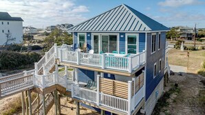 En toetagers strandhus med balkon, træterrasse og trappe op til øverste etage.