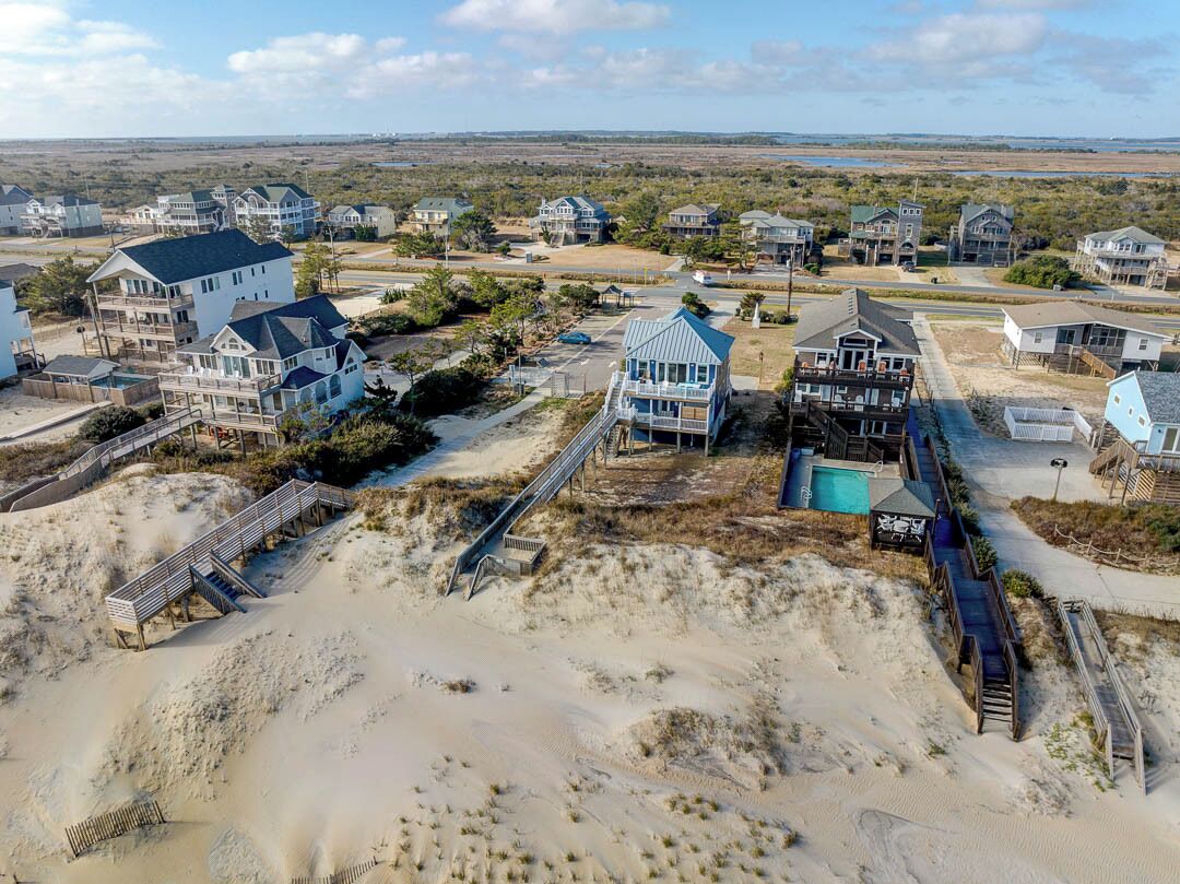 Un quartier résidentiel situé sur la côte, avec des maisons, un terrain sablonneux et un chemin d’accès à la plage.